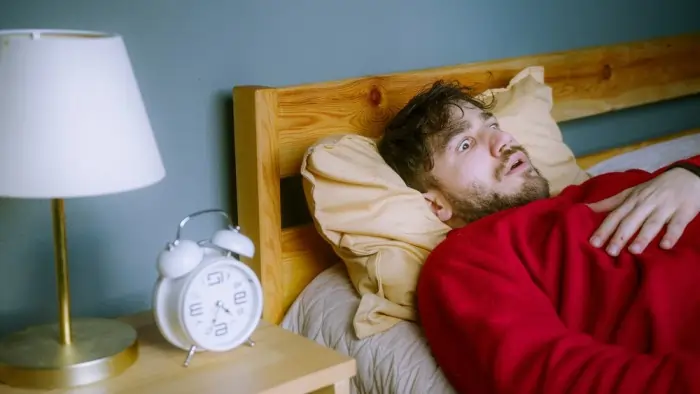 A man lying in bed with wide eyes and his hand on his chest, vividly illustrating a state of intense anxiety during sleep paralysis.