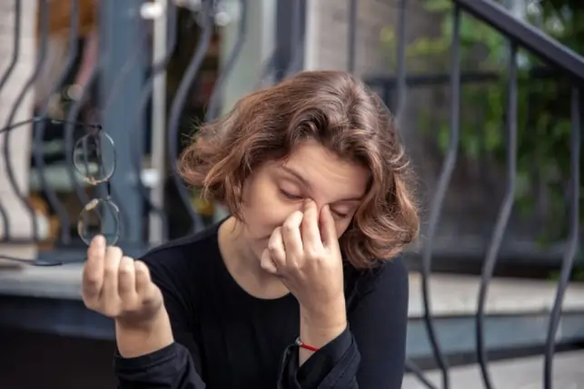 Stressed woman holding glasses and rubbing her eyes to show the link between anxiety and blurred vision.