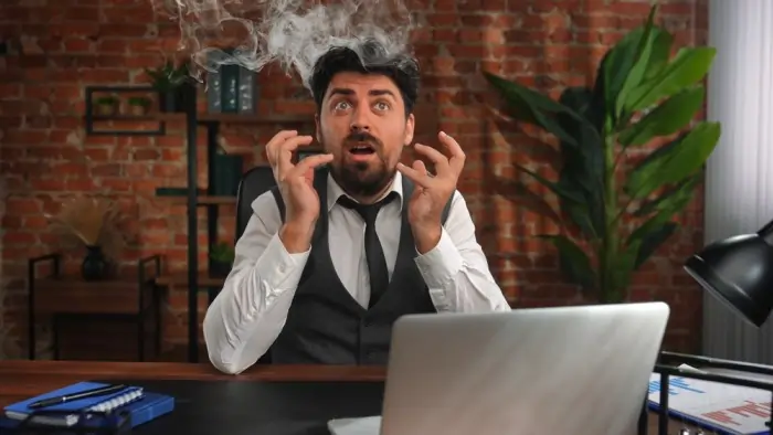 Burnout anxiety depicted by a stressed businessman at a desk with smoke rising from his head.