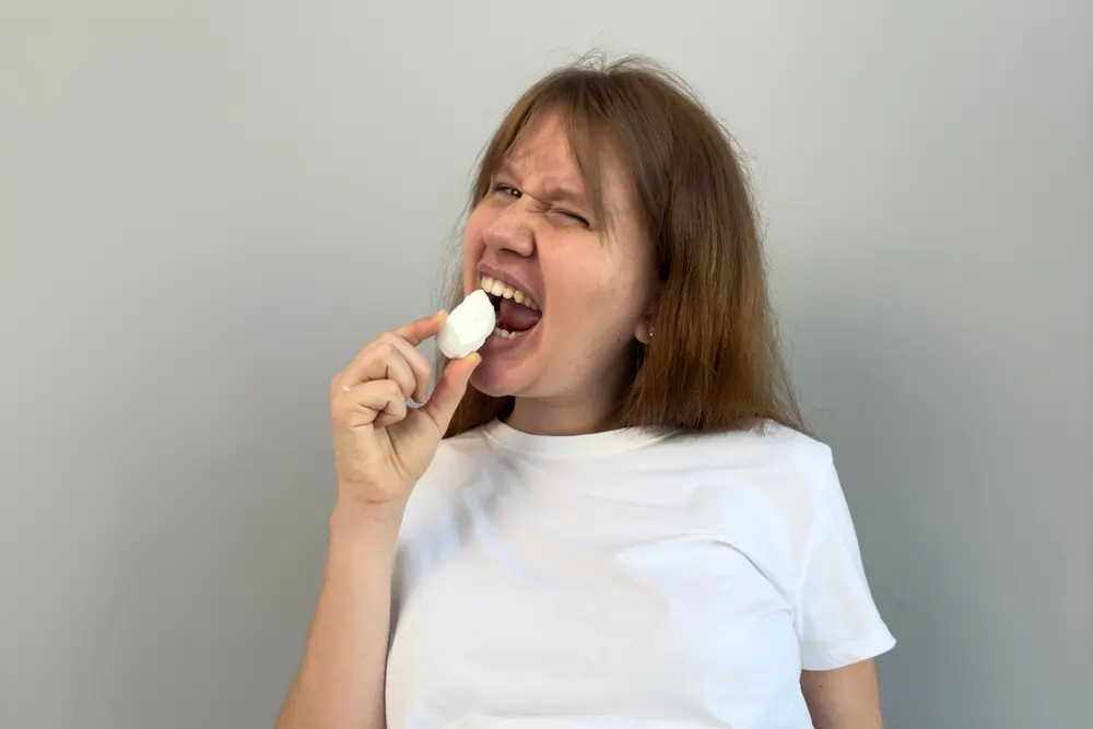 Woman biting on chalk, illustrating the dental and health consequences of chalk eating addiction in adults.