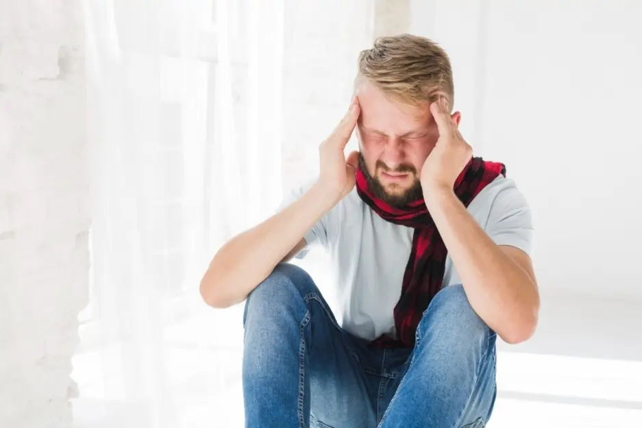 Man holding head in pain showing anxiety and physical ailments, stress headache and mental health discomfort at home indoors