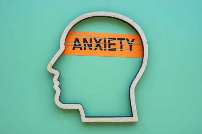 A wooden head silhouette with an orange 'ANXIETY' band across the mind, visually capturing the concept of inhibition and anxiety.