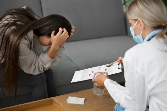 Woman experiencing anxiety and emotional distress during a therapy session, while a healthcare professional provides support. The image highlights the relationship between inhibition, anxiety, and treatment strategies for managing symptoms and improving mental health.