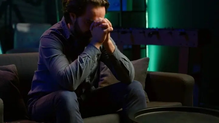 A stressed man sitting on a couch, showing signs of anxiety about the future and feeling overwhelmed by worry.