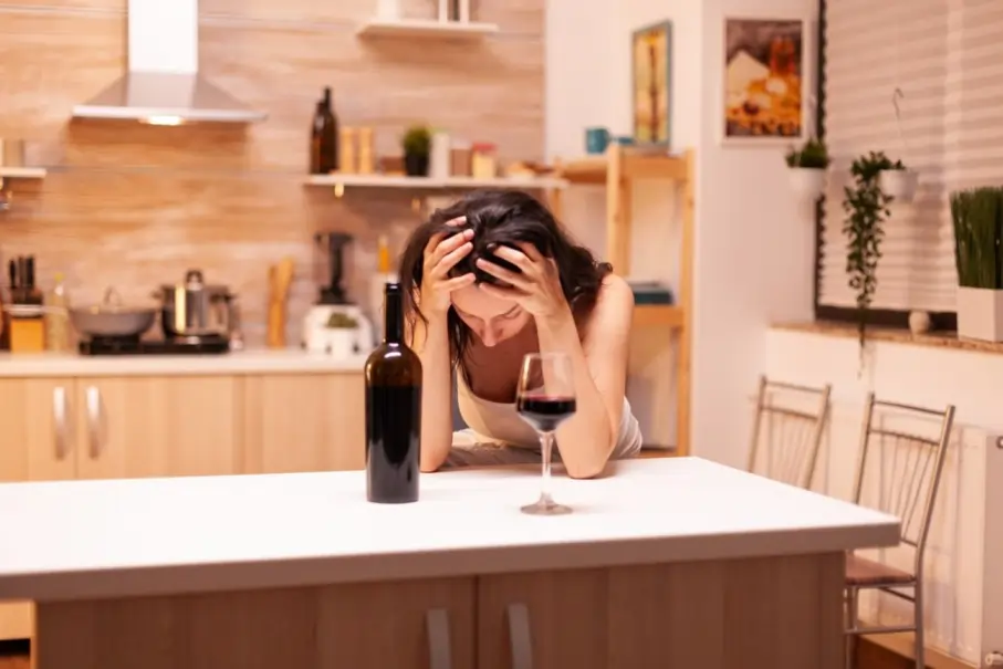 Distressed woman in a kitchen with wine, illustrating the psychological factors behind women and alcohol addiction.