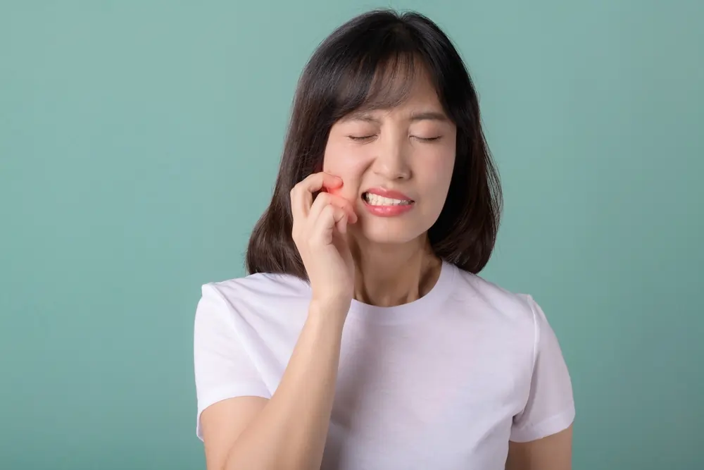 A woman holding her jaw in pain, illustrating common molar cavity signs like toothaches and sensitivity to heat or cold against a teal background.