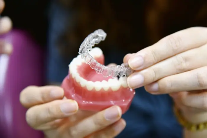 Hands holding a clear plastic orthodontic aligner over a dental model to demonstrate how a new tray fits during teeth straightening treatment.