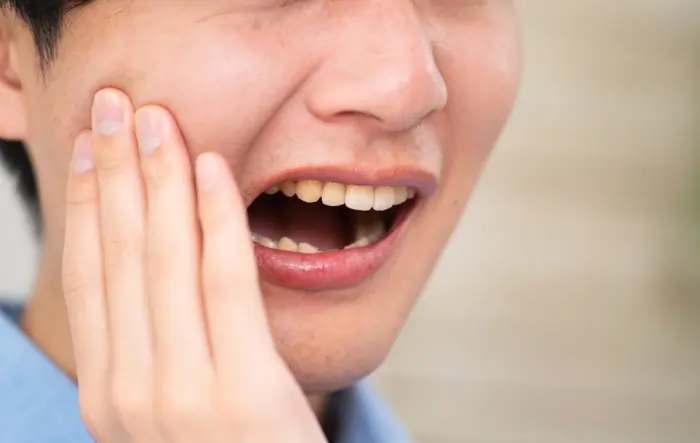 man holding jaw with wisdom tooth pain caused by tooth decay and cavity infection