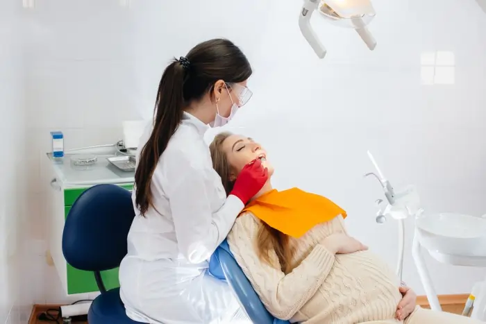 A pregnant woman receiving professional tooth decay treatment from a dentist in a clinical office setting.