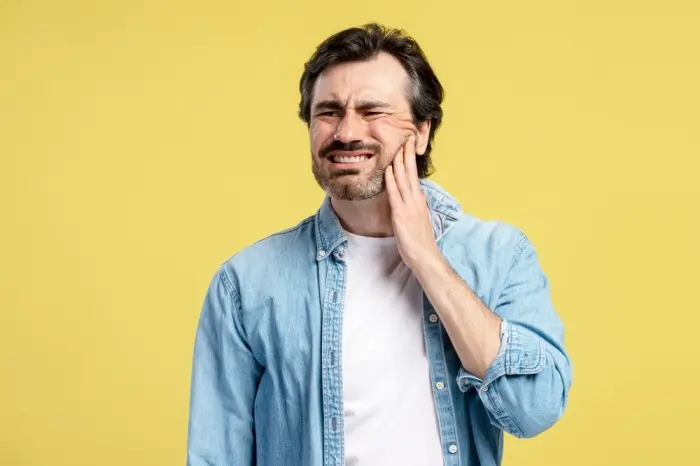man holding jaw in pain due to wisdom tooth decay infection and dental inflammation