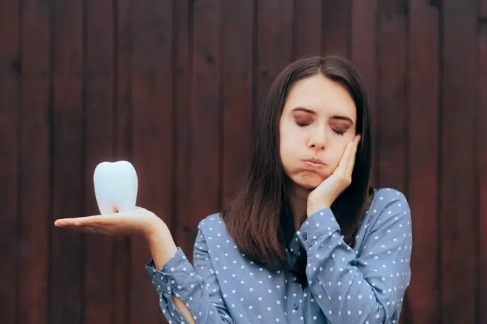 Woman holding a tooth model with cheek pain expression representing wisdom tooth decay signs and dental discomfort.