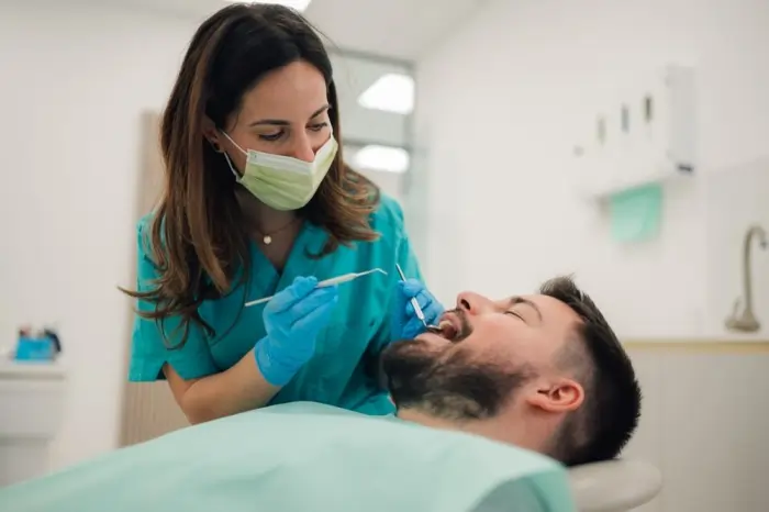 Hand holding models of teeth with different levels of decay and a toothbrush, visualizing why a cavity filling is needed to stop progression.