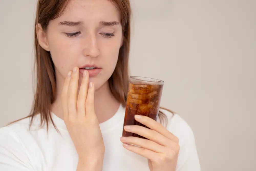 Young woman experiencing sharp tooth pain from a cold drink, illustrating how and when a cavity starts hurting.